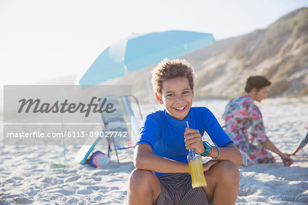 Portrait smiling, confident boy drinking juice on summer sunny beach