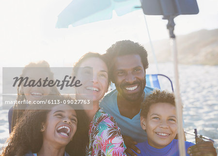 Happy, playful multi-ethnic family taking selfie with selfie stick on sunny summer beach