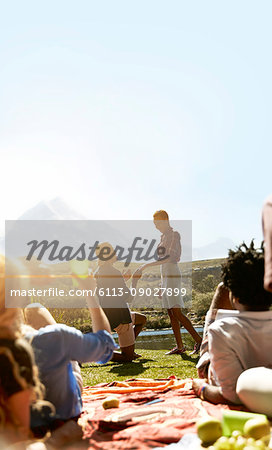 Friends watching young man proposing to woman at sunny summer picnic