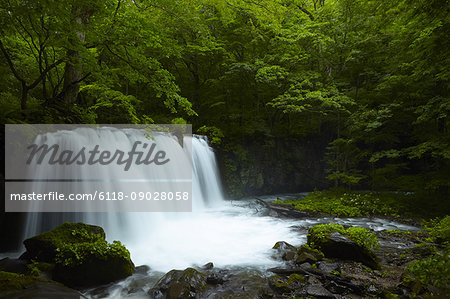 Long exposure of rocky waterfall surrounded by trees with lush green foliage.