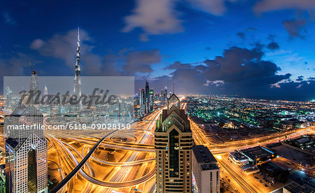 Cityscape of Dubai, United Arab Emirates at dusk, with the Burj Khalifa and other skyscrapers and illuminated highway in the centre.