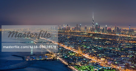 Cityscape of Dubai, United Arab Emirates at dusk, with skyscrapers lining coastline of the Persian Gulf.