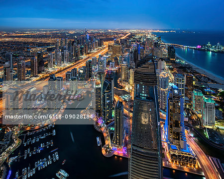 Aerial view of the cityscape of Dubai, United Arab Emirates at dusk, with illuminated skyscrapers and the marina in the foreground.