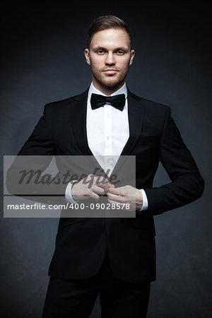 Young handsome businessman in black suit on gray background