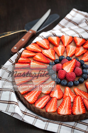 Delicious chocolate tart decorated with fresh strawberry, blueberry and raspberry