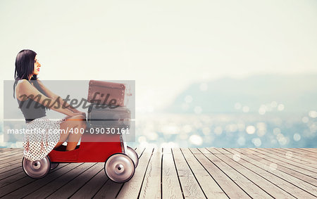 Girl ready to travel with a small car full of baggages with a bright sea on background
