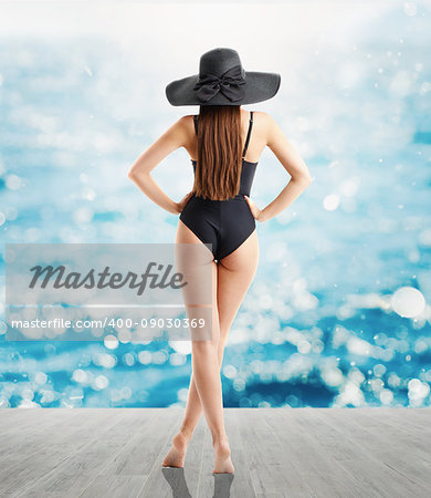 Woman in elegant black straw hat and swimsuit looks at sea