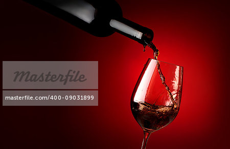 Red wine pouring in a wineglass on a red background