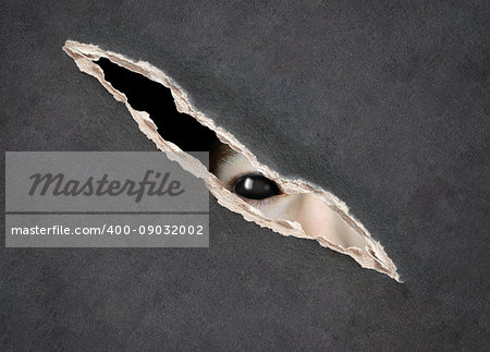 Halloween background with paper texture of grey color and monster eye in hole in the paper. Look from darkness.