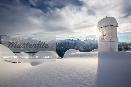 Winter sun shining behind the pictoresque bell tower at Alpe Scima after an heavy snowfall. Valchiavenna, Valtellina Lombardy Italy Europe