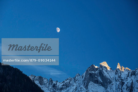 The moon on the snowy mountains illuminates the peaks at sunset Bondasca Valley Switzerland Europe