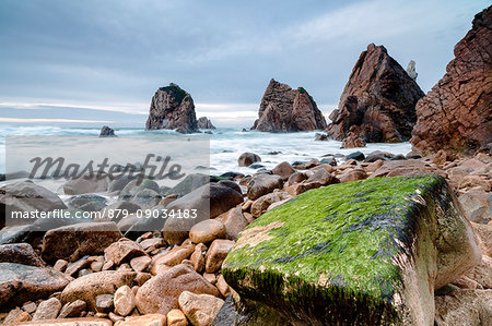 Ocean waves crashing on stones of Praia da Ursa beach surrounded by cliffs Cabo da Roca Colares Sintra Portugal Europe