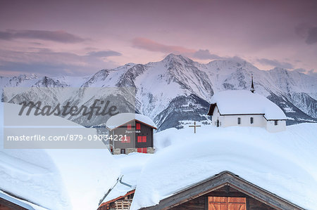 Pink sky at sunset frames the snowy mountain huts and church Bettmeralp district of Raron canton of Valais Switzerland Europe
