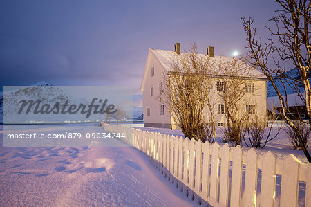 Full moon and lights on the typical wooden house surrounded by snow Flakstad Lofoten Islands Northern Norway Europe