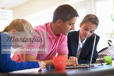 Father helping daughters with homework at kitchen counter