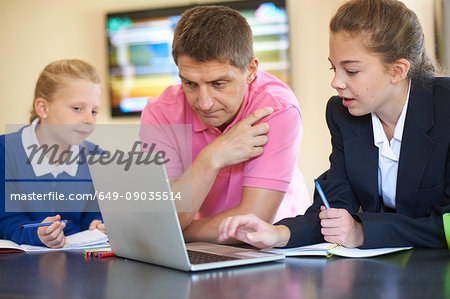 Father helping daughters with homework at kitchen counter
