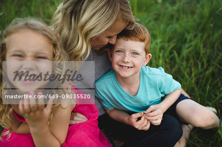 Portrait of girl and brother sitting on mothers lap in grass