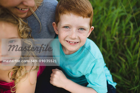 Portrait of girl and brother sitting on mothers lap in grass