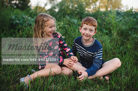 Girl and brother sitting in field