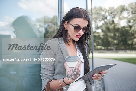 Businesswoman outdoors, holding coffee cup and digital tablet, tattoos on hands