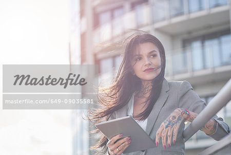 Businesswoman outdoors, holding digital tablet, tattoos on hands