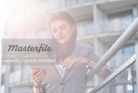 Businesswoman outdoors, using digital tablet, tattoos on hands