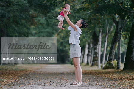 Woman holding up baby daughter in tree lined park, Chenonceaux, Loire Valley, France