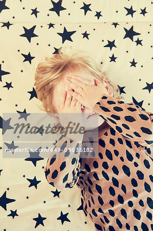 Female toddler lying on star pattern bed with hands covering eyes