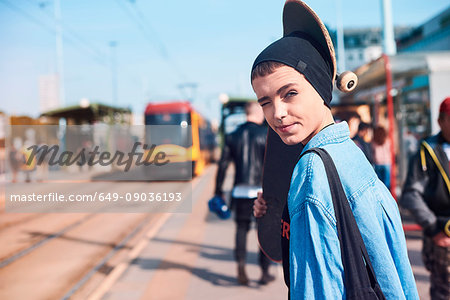 Portrait of cool young female skateboarder in beanie hat at tram station