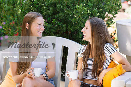 Two young female friends chatting over coffee at sidewalk cafe
