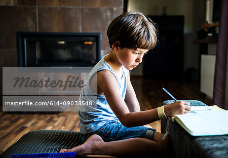Boy kneeling on floor drawing in workbook