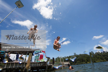 Teenagers jumping into lake, low angle view