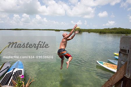 Mature man jumping into water, mid air