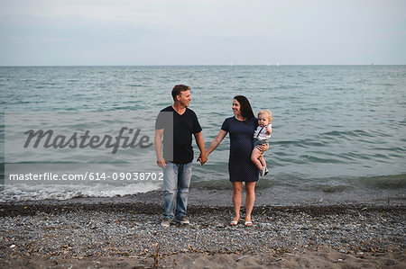 Pregnant couple at water's edge on beach with male toddler son, Lake Ontario, Canada