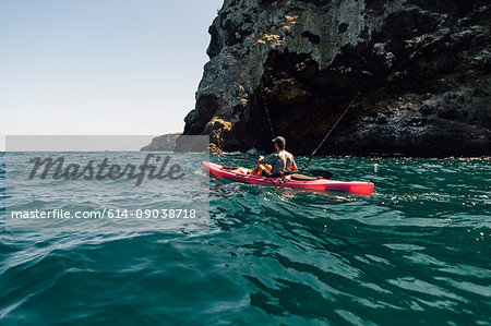 Young male sea kayaker fishing near cliff, Santa Cruz Island, California, USA