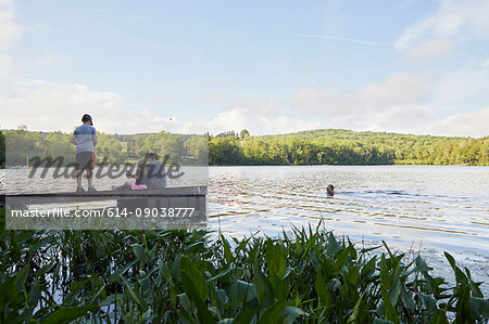 Three children on jetty, father swimming in lake