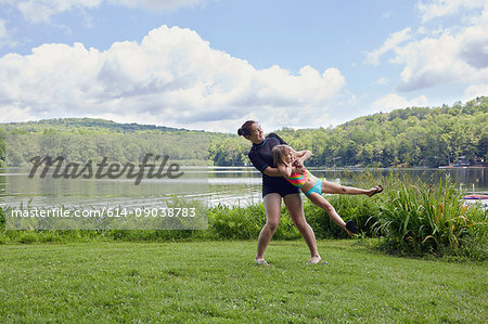 Girl swinging young girl around on grass, beside lake