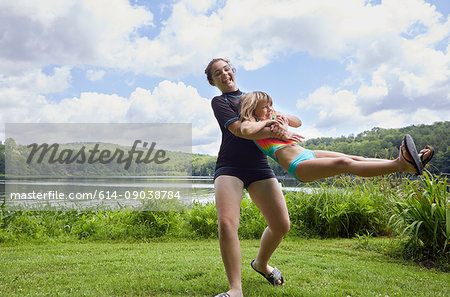 Girl swinging young girl around on grass, beside lake