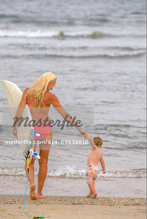 Rear view of woman surfer at water's edge with toddler daughter, Asbury Park, New Jersey, USA