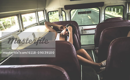 Young woman sitting on a bus with a surfboard.