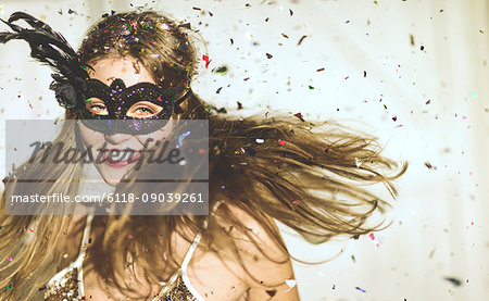 Young woman wearing a black eye mask at a party with confetti falling.