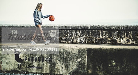 Young woman walking on a wall bouncing a basketball.
