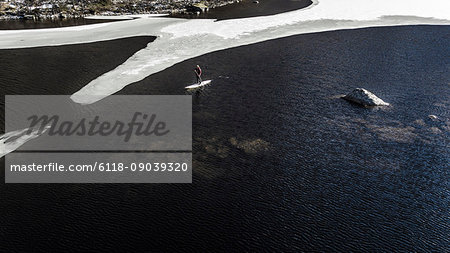 Aerial view of a paddleboarder on the water in an inlet with melting ice floes in the Lofoten Islands, Norway.