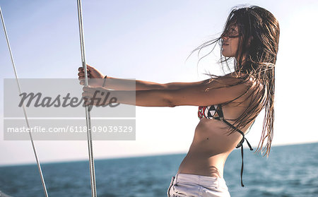 A young woman on board a yacht, side view in bikini and shorts.