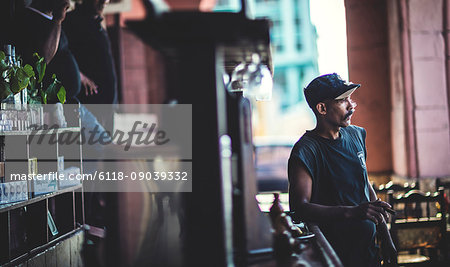 A man leaning on the bar in a cafe holding a large cigar.