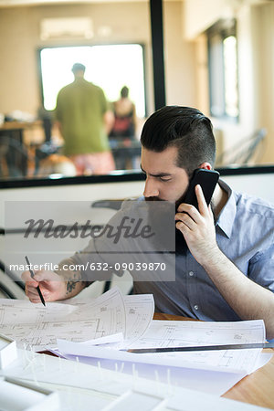 Man talking on cell phone and looking at blueprints in office