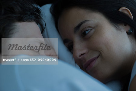 Young woman lying in bed looking at boyfriend sleeping