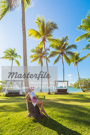 Playa Moron, Las Terrenas, Samana Peninsula, Dominican Republic. Woman relaxing on a palm-fringed meadow (MR).