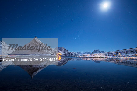 Full moon and stars light up the snow capped peaks reflected in sea Volanstinden Fredvang Lofoten Islands Northern Norway Europe