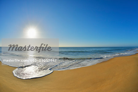 Surf breaking on the shoreline of Ninety Mile Beach at Paradise Beach with the sun shining over the ocean in Victoria, Australia